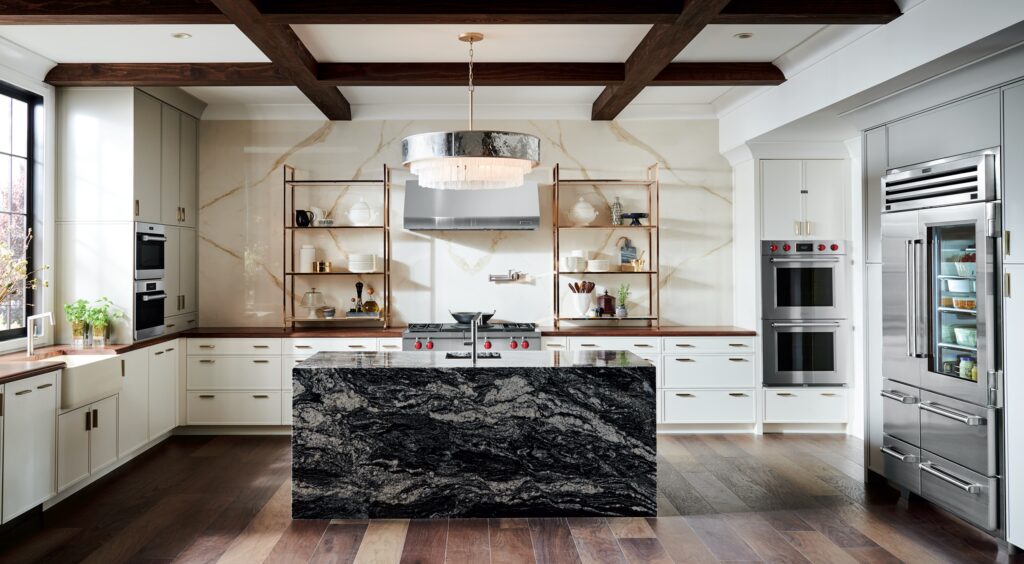 Modern luxury kitchen with marble walls, a large island with a black granite countertop, high-end Wolf cooking appliances, and a SubZero refrigerator.